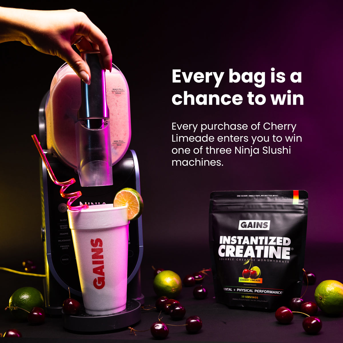 A hand inserts a capsule into a black and pink Gains Instantized Creatine machine, which dispenses a drink into a white Gains cup. A black bag of Gains Instantized Creatine is shown next to the machine on a dark background with cherries and limes scattered around | cherry limeade
