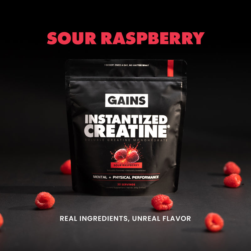 Black package of 'Gains Instantized Creatine' with sour raspberry flavor on a dark background with raspberries. | sour raspberry 30