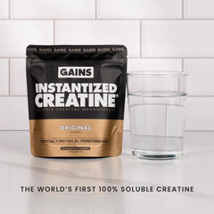 GAINS Instantized Creatine package with a glass of water on a white surface. | original