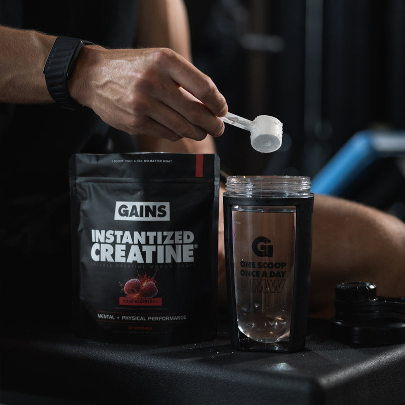 Person measuring creatine powder with a scoop from a GAINS package. | sour raspberry 30